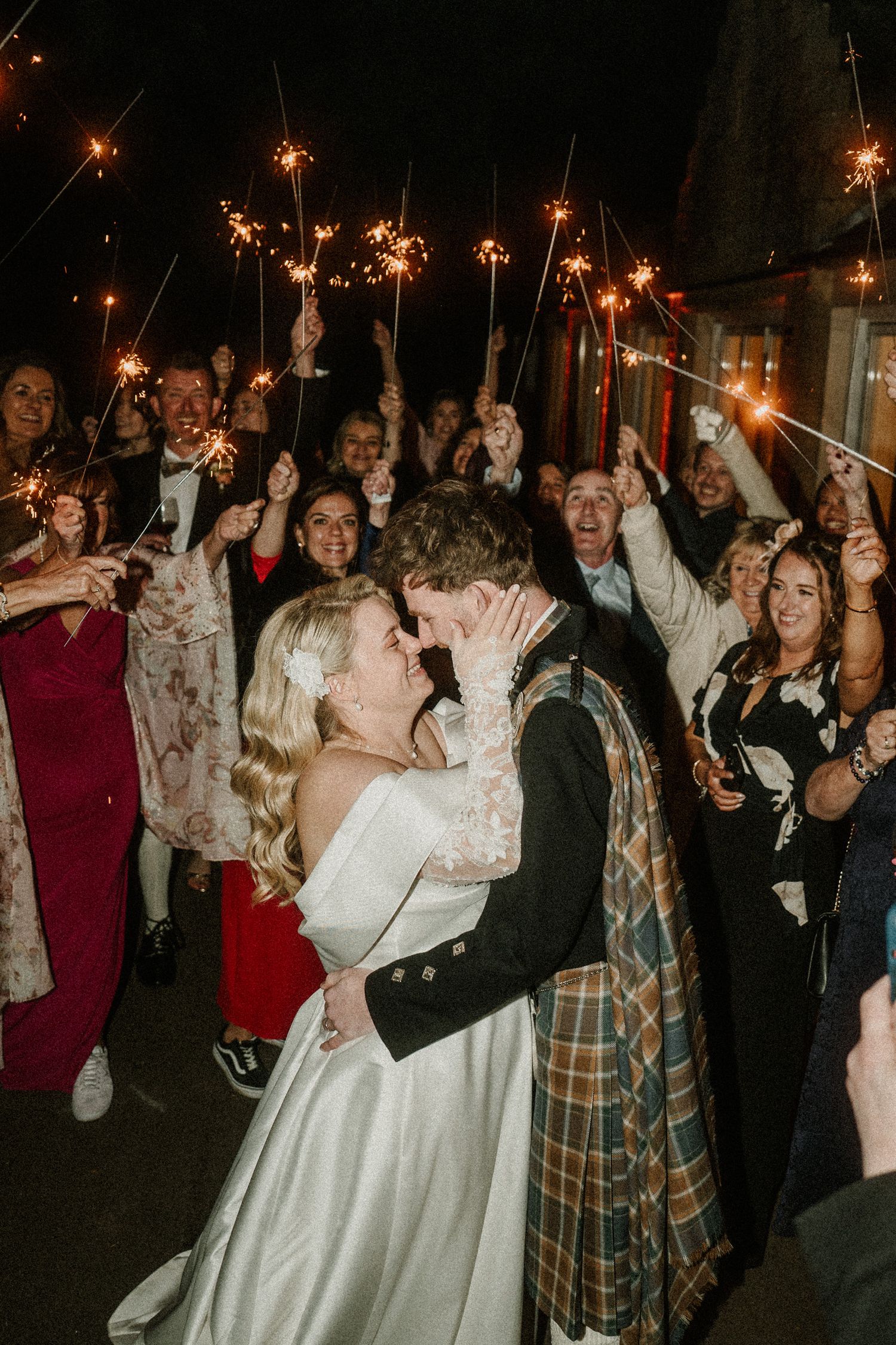 Nighttime wedding celebration with guests holding sparklers while the newlyweds celebrate.