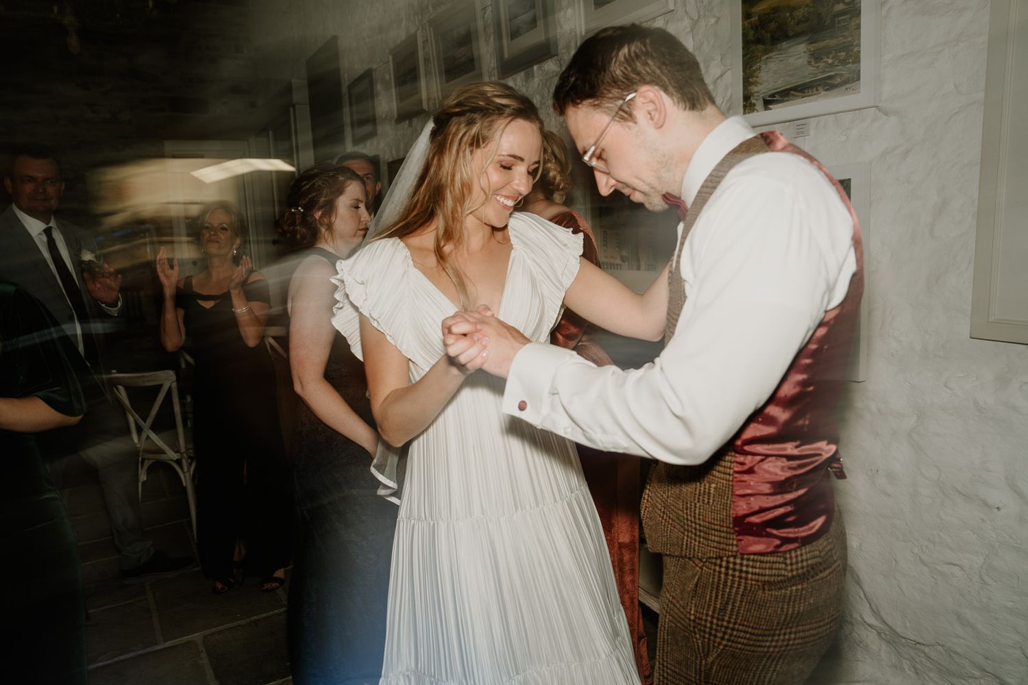 A couple dances together in an intimate rustic venue with white stone walls.