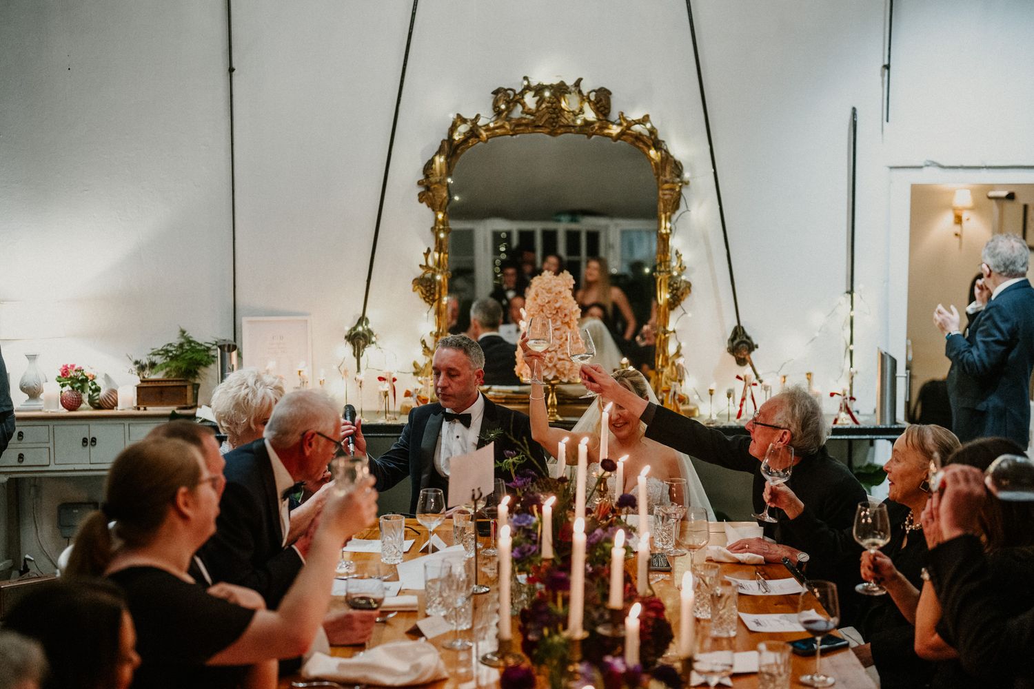 Elegant dinner party setup with candlelight, gold mirrors, and guests raising glasses in celebration.