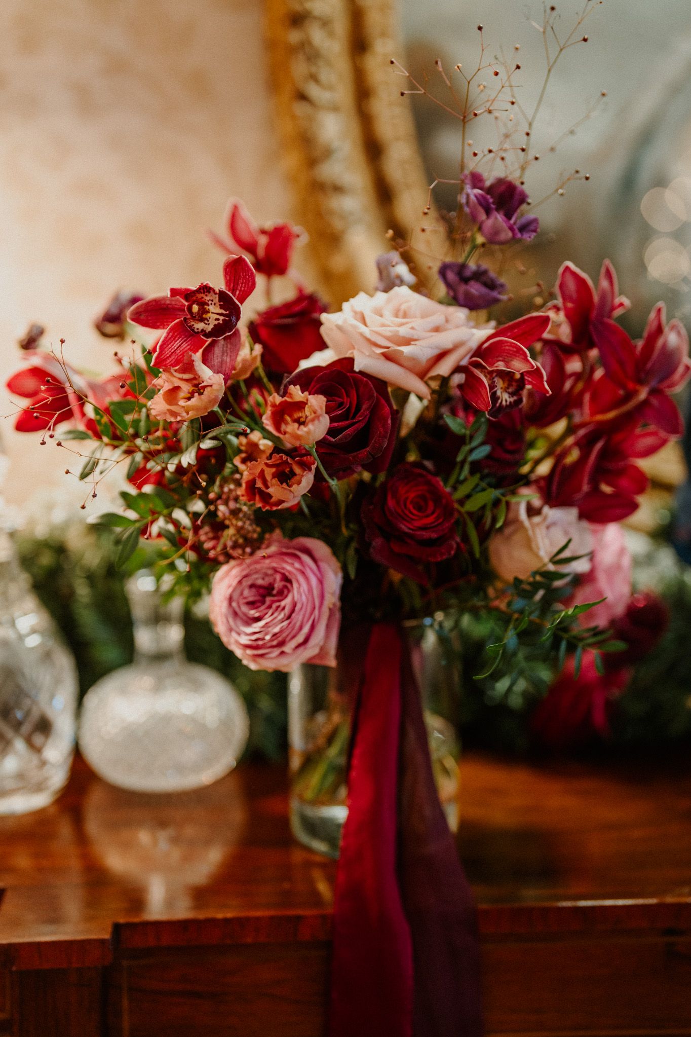 Vibrant floral arrangements with red and pink roses adorned with burgundy ribbons on a wooden surface.