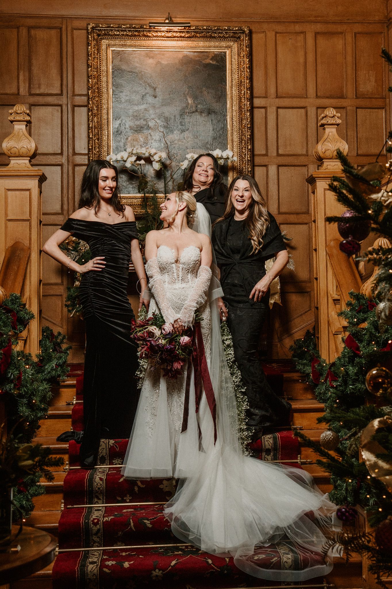 Wedding party poses on elegant staircase with wood paneling and holiday decorations.