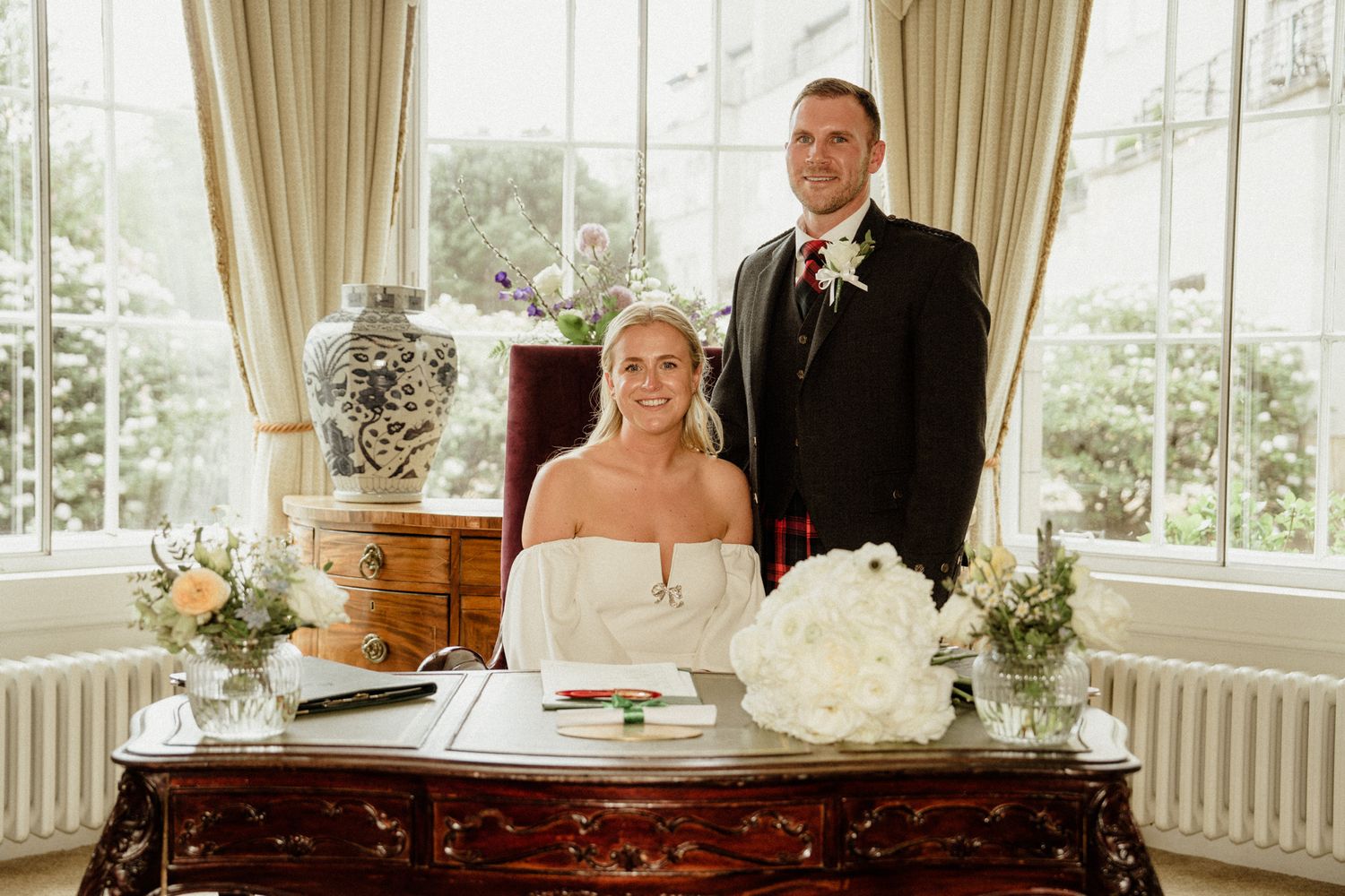 Wedding celebration in an elegant sunlit room with large windows and flowing curtains.