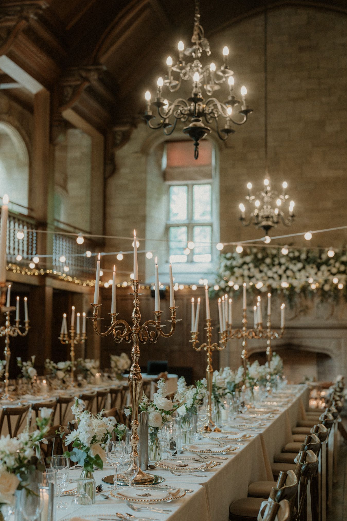 Long banquet table set with candelabras and flowers under dramatic chandelier lighting at Achnagairn Castle in Scotland.