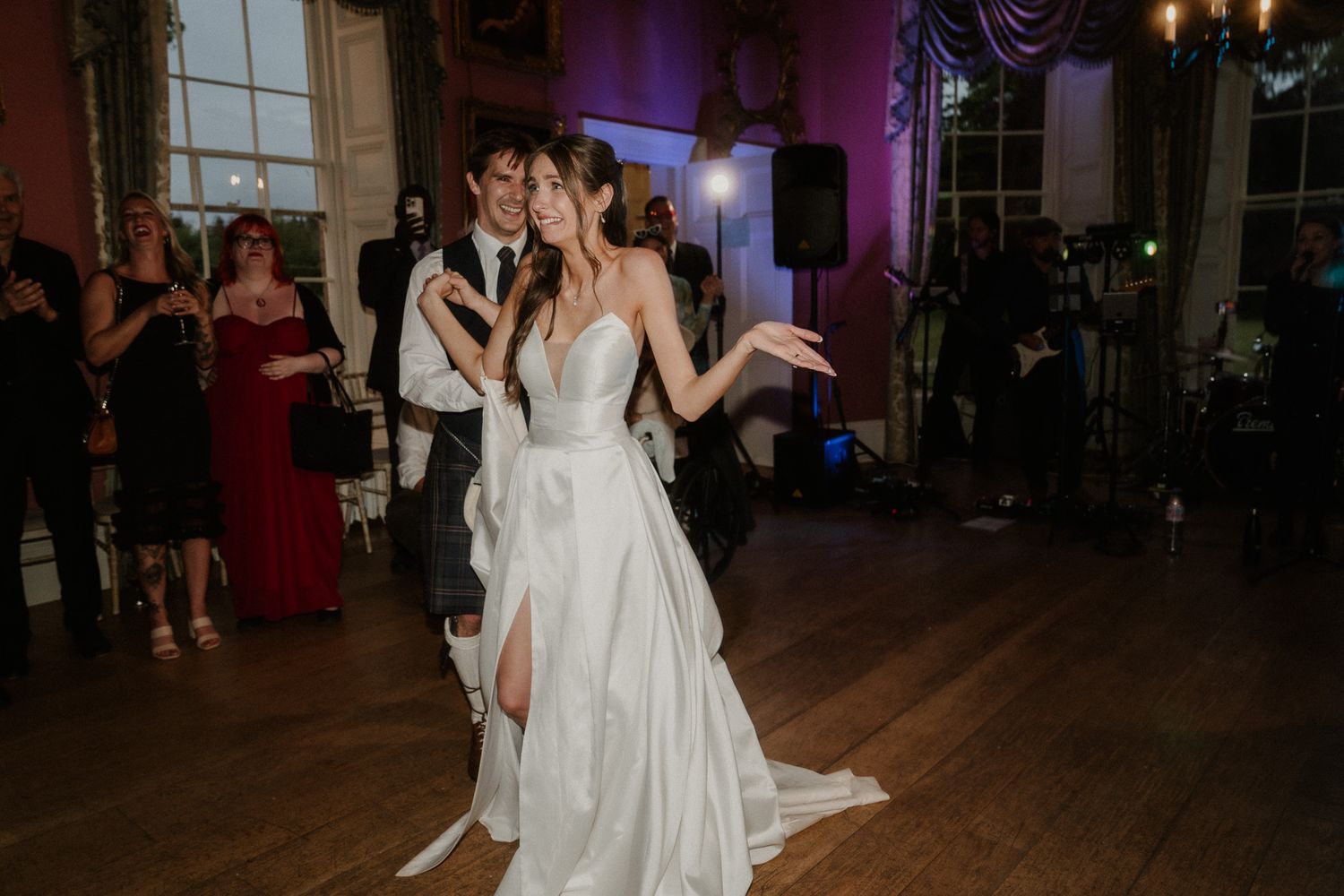 Bride in white satin gown dancing with groom during wedding reception on elegant ballroom dance floor.