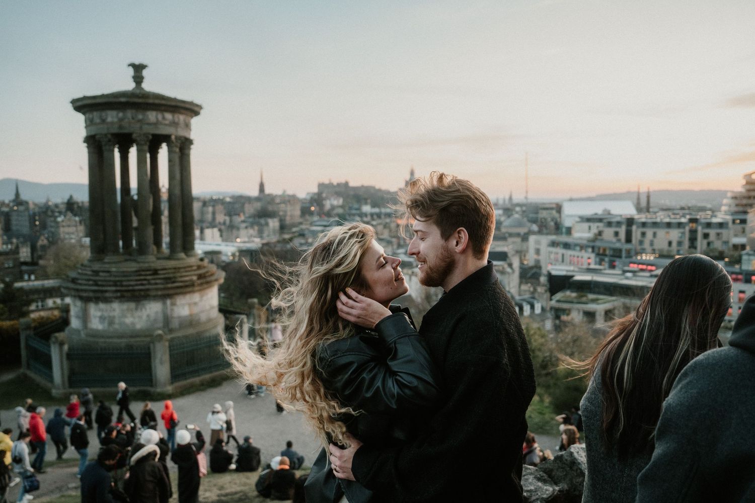 Couple sharing a romantic moment at Calton Hill Edinburgh with city skyline at dusk.