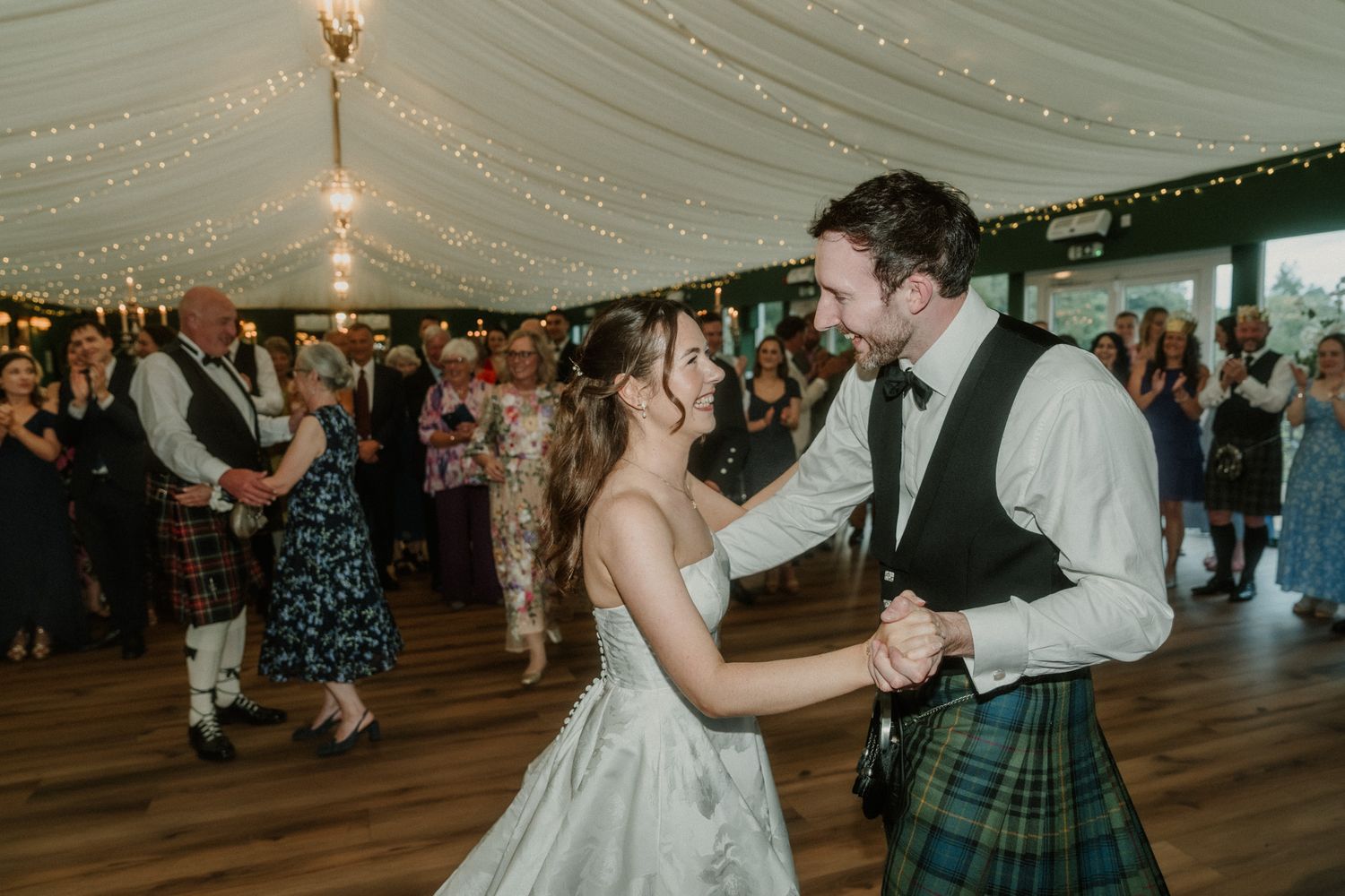 Bride and groom share first dance in Scottish wedding marquee, groom wearing traditional tartan kilt.