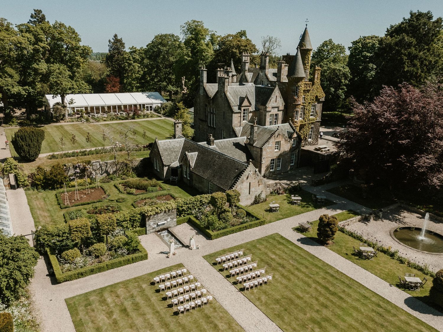Aerial view of an outdoor wedding ceremony setup with white chairs on a manicured lawn beside a stone church.