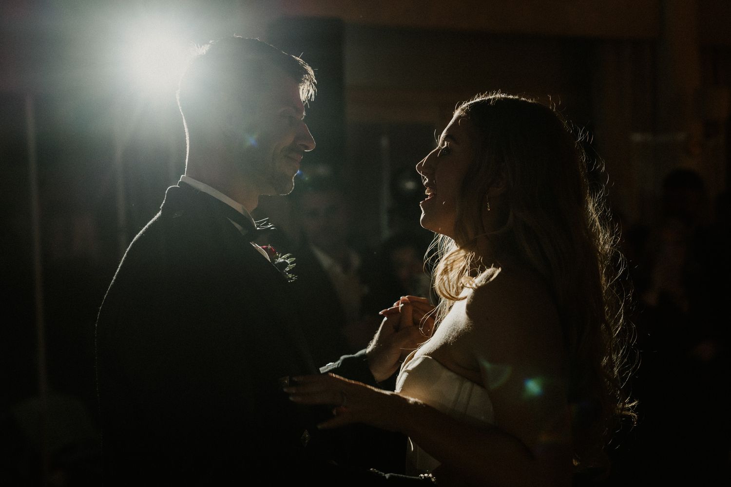 Dramatic side-lit profile shot of someone singing or performing at a nighttime event.