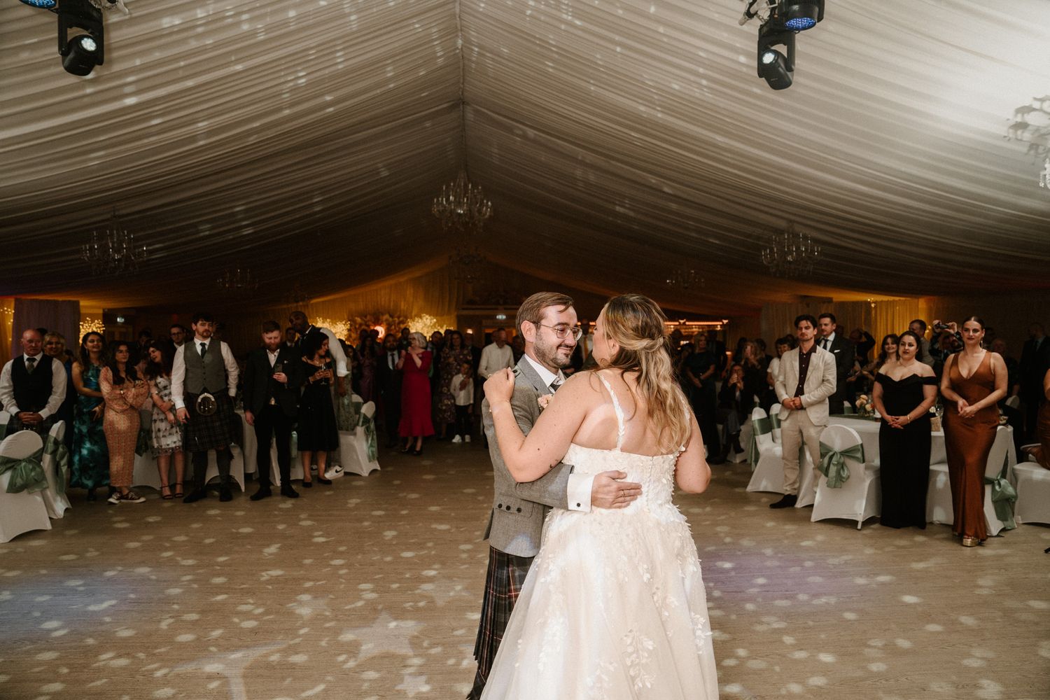 Elegant wedding venue with white tent ceiling and guests dancing on the floor.
