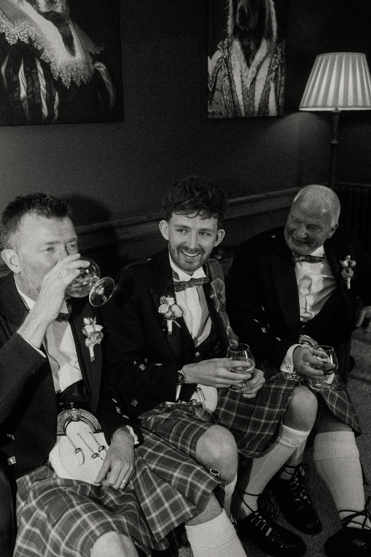 Black and white photo of three men in kilts enjoying drinks together.