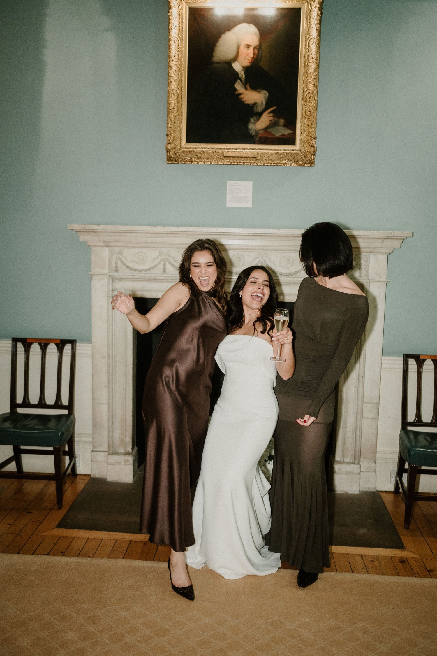 Wedding party members in formal attire dance and celebrate in an elegant room with mint green walls.