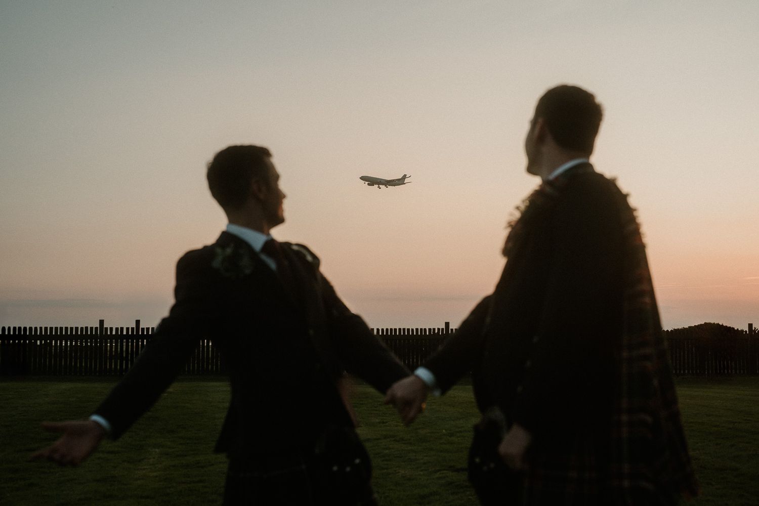 Silhouettes of people against a sunset sky with an airplane flying overhead.