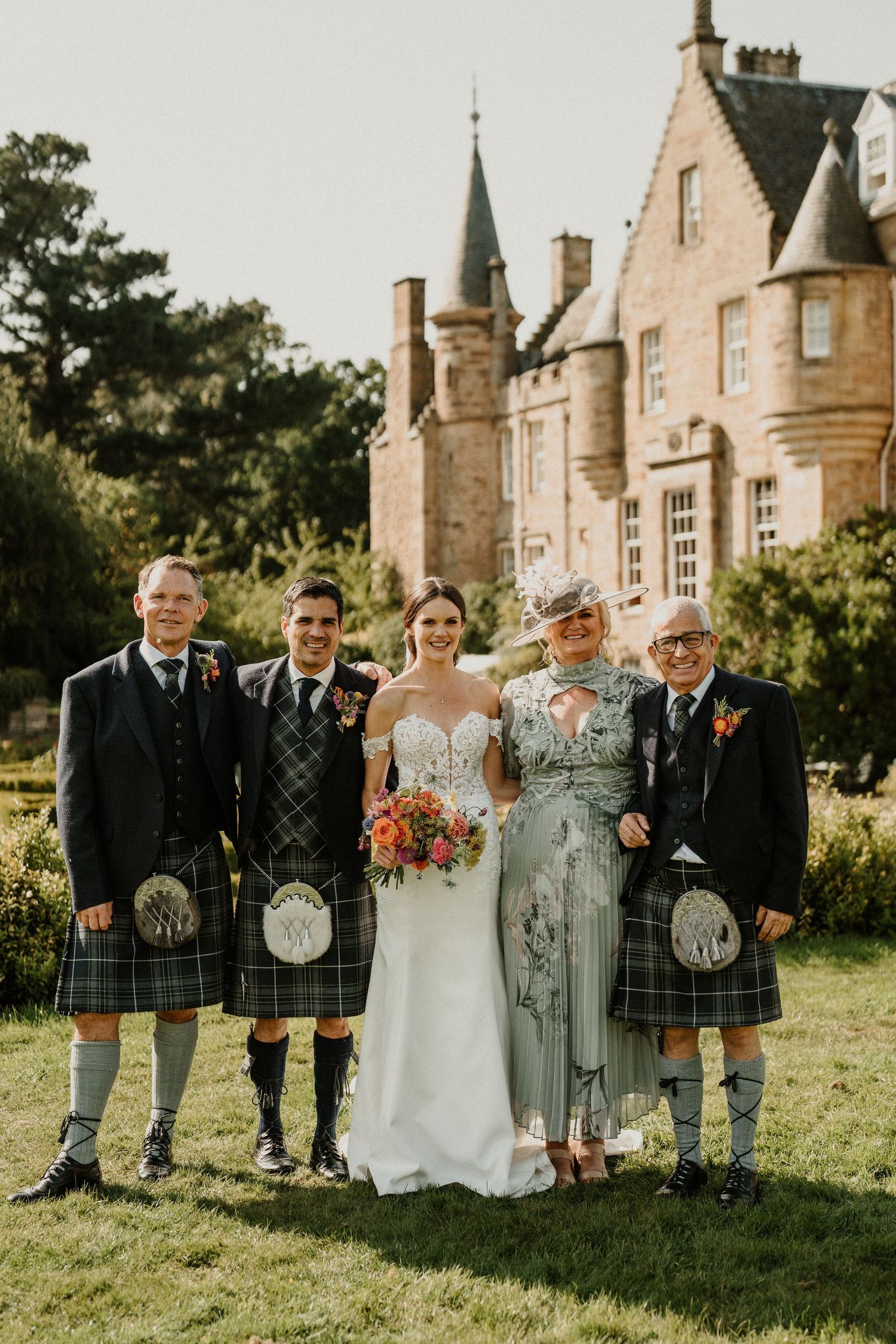 Family wedding portrait with Scottish attire in front of historic stone castle.
