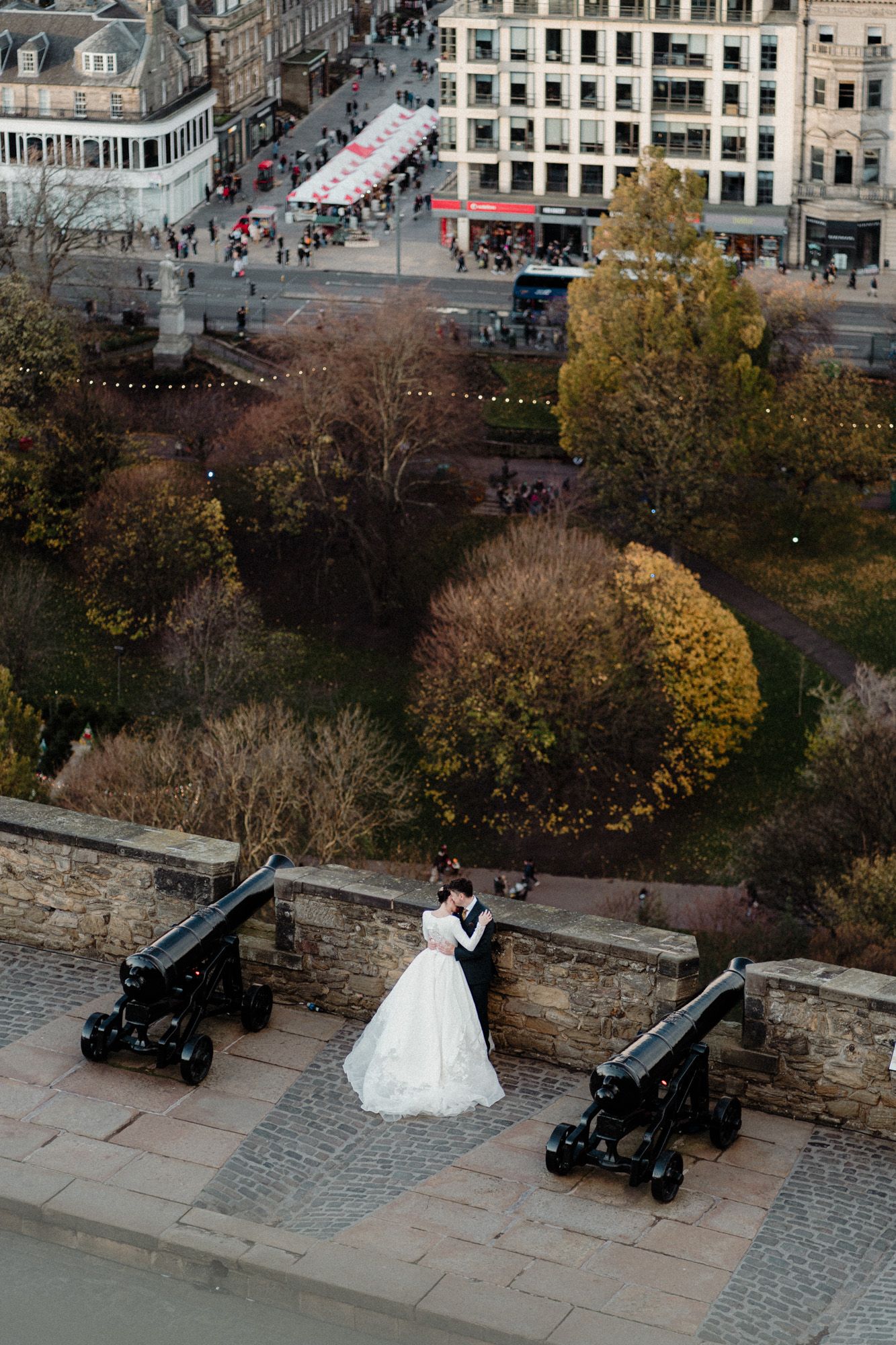 Aerial view of a wedding photo session with a white dress against stone architecture and autumn trees.