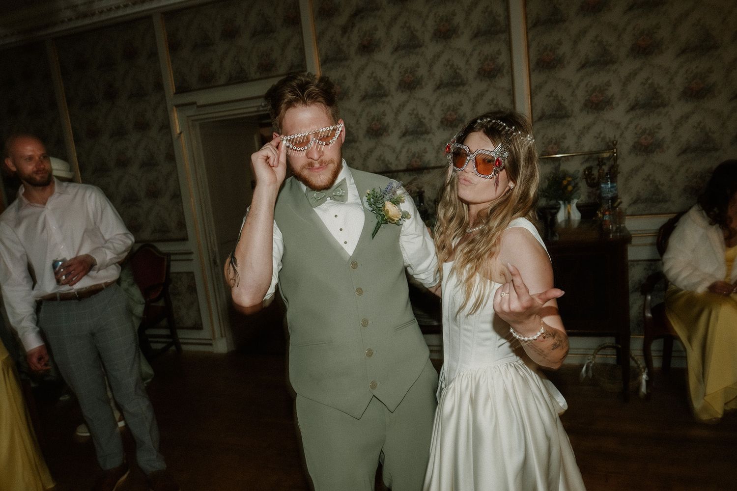 Bride and groom dancing at wedding reception wearing fun oversized sunglasses in elegant venue.