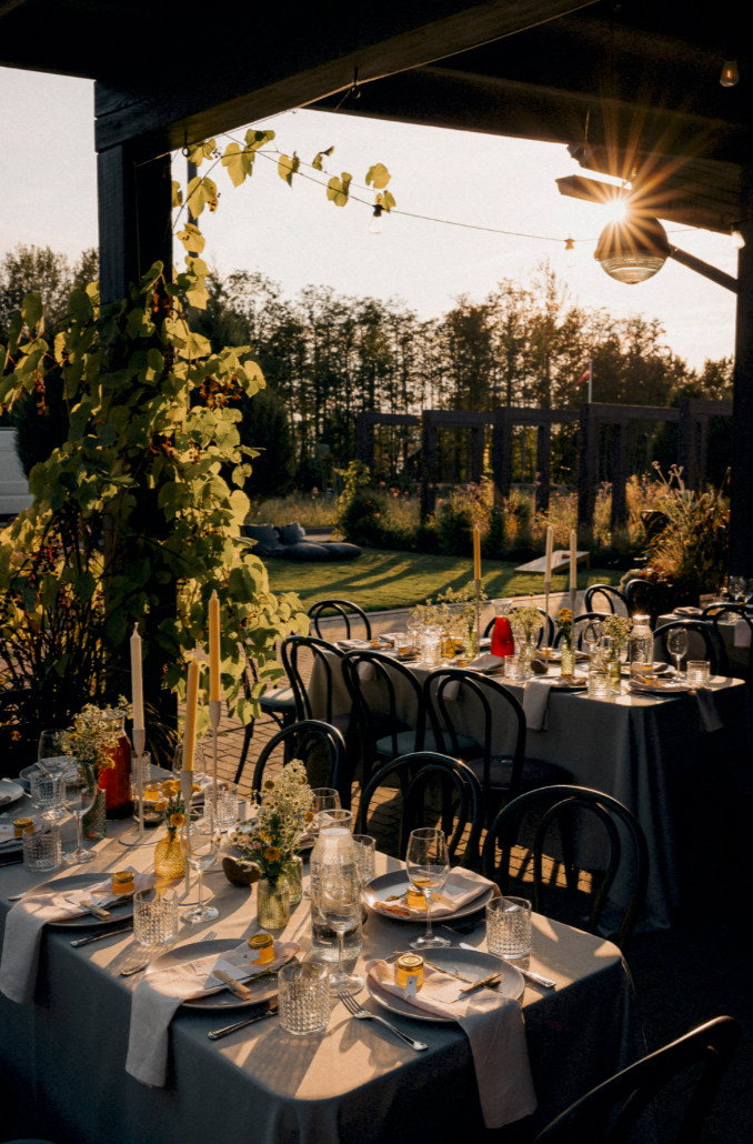 Elegant outdoor wedding reception with set tables, candles, glassware, and lush greenery at golden hour sunset.