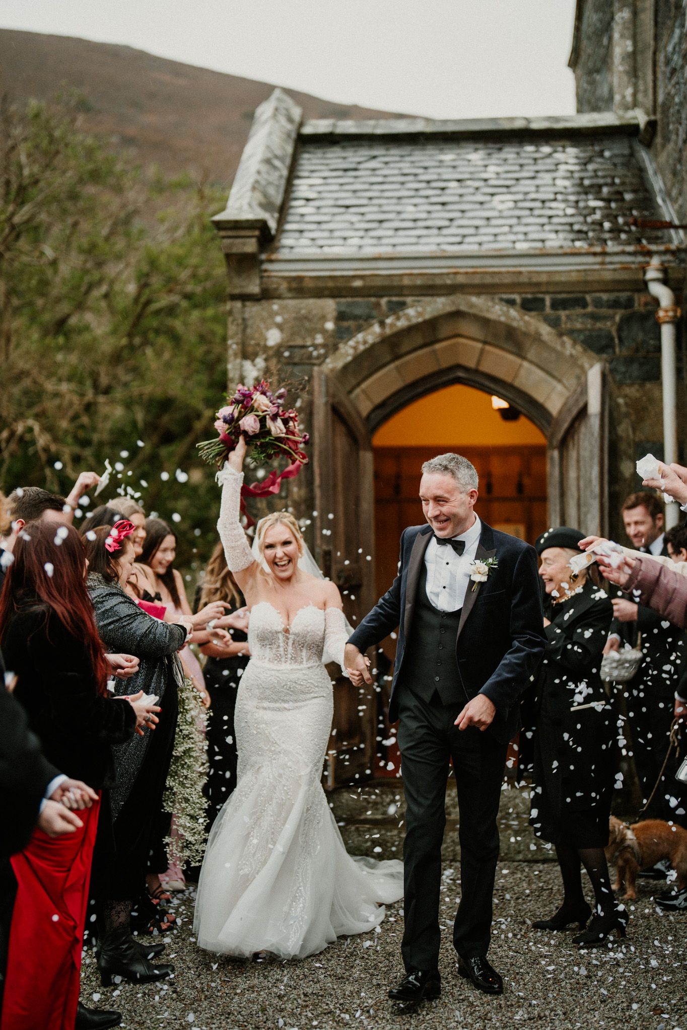 Celebratory confetti toss as wedding couple exits historic stone church.