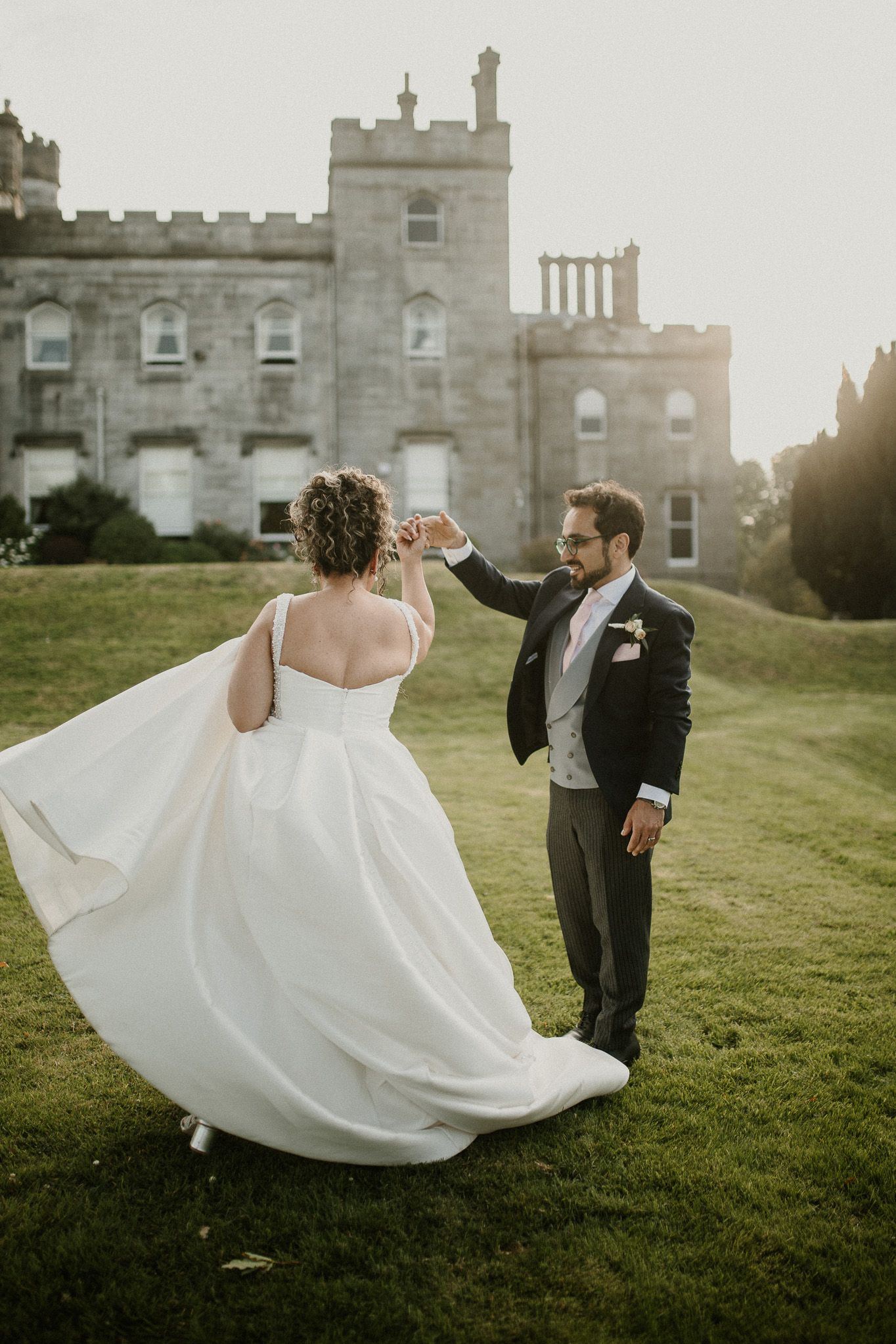 Couple dances on castle lawn during golden hour wedding celebration.