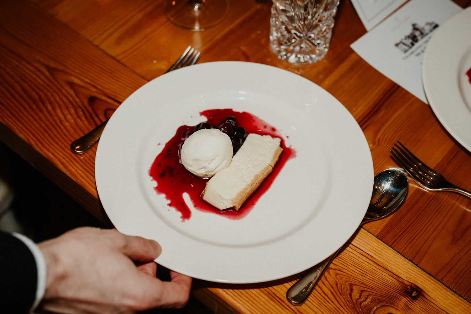 White plates with red accents arranged on a wooden dining table at an elegant event.