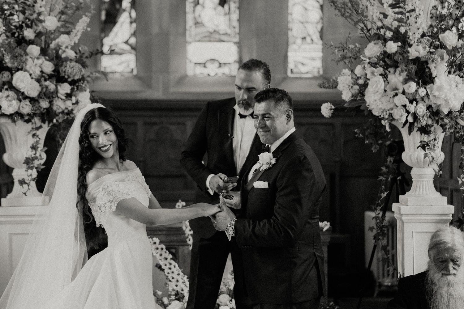 A wedding ceremony takes place in a church decorated with elegant white floral arrangements.