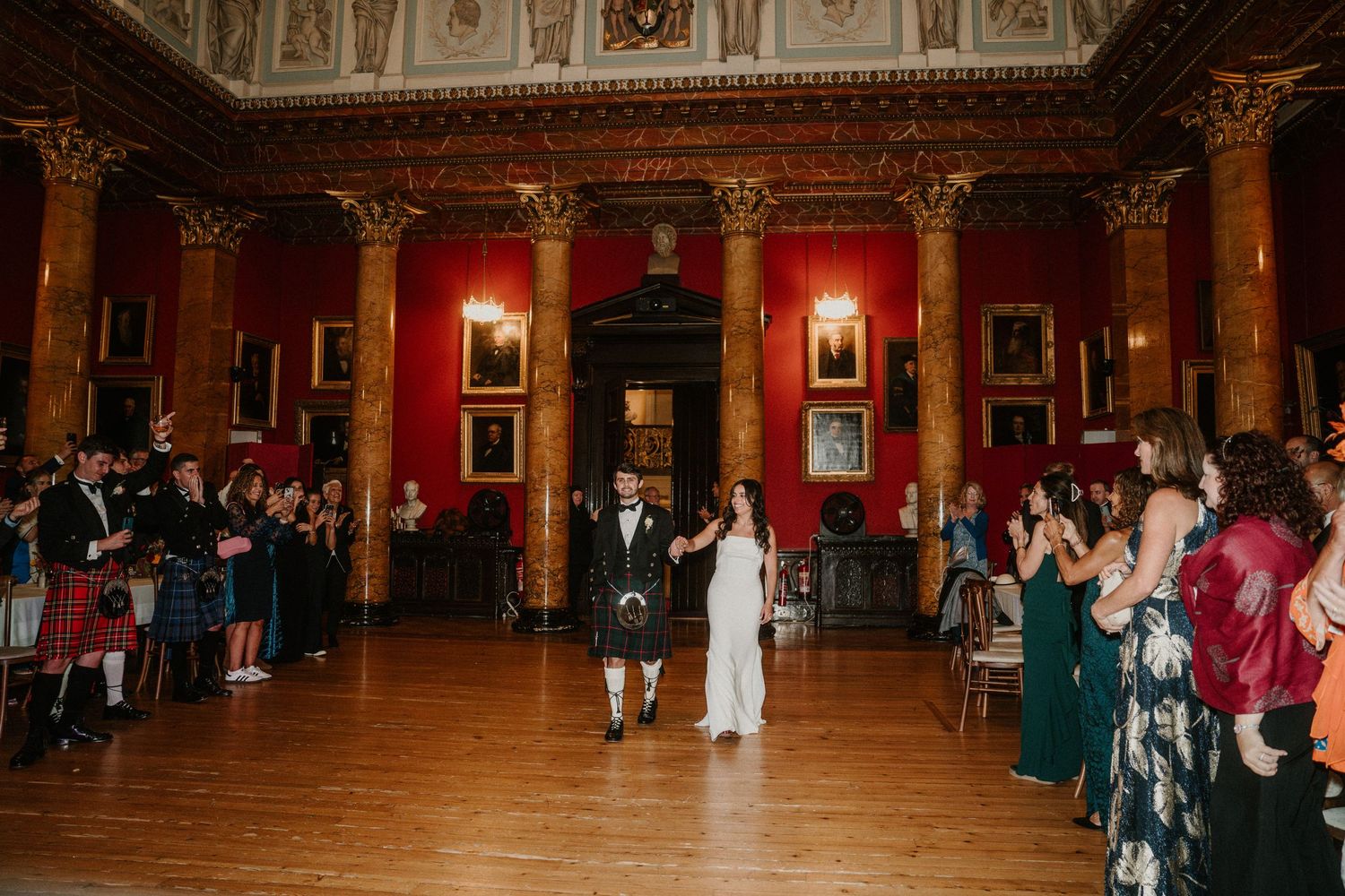 Wedding celebration in a grand ballroom with ornate ceiling details and red walls.