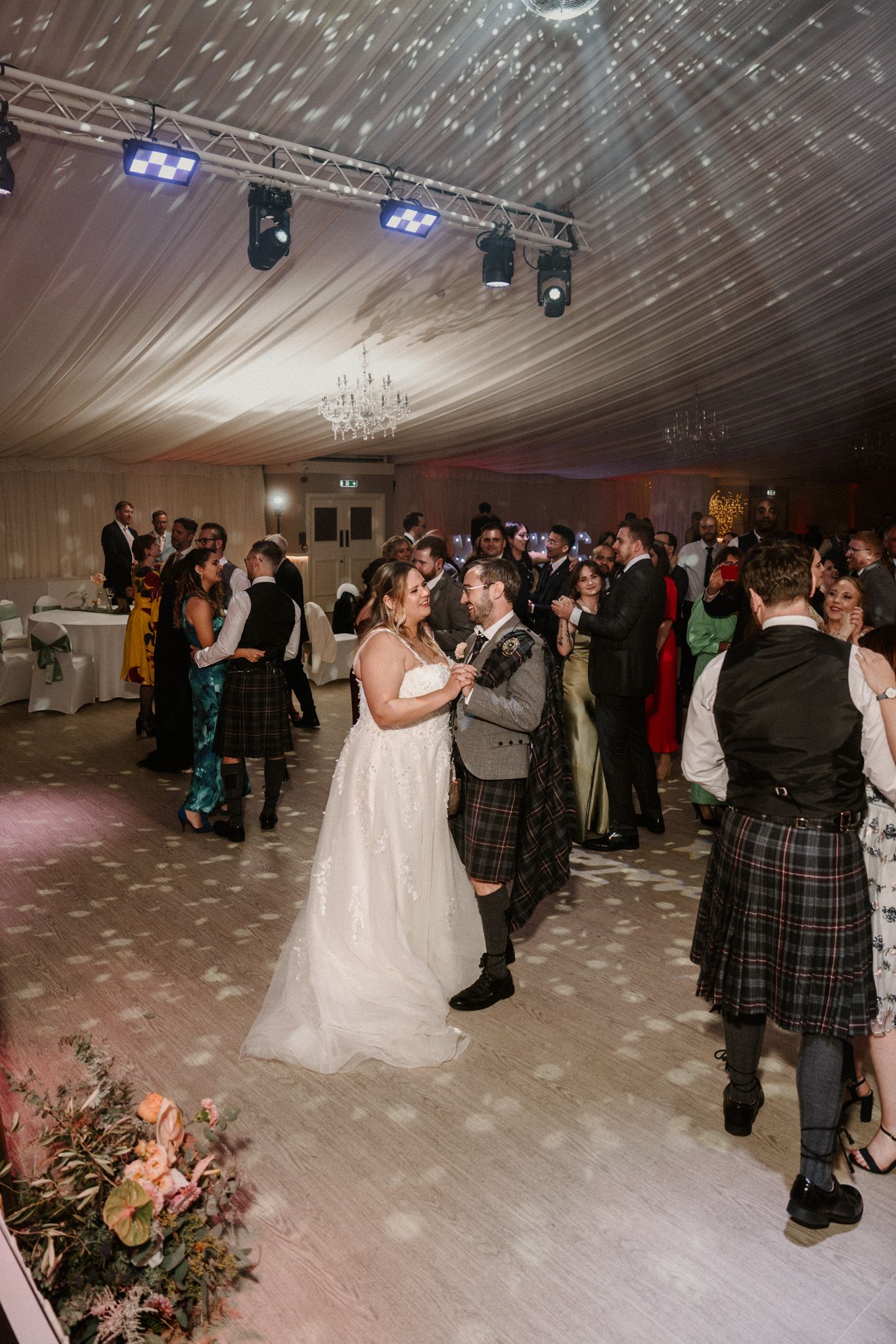 Wedding celebration with traditional Scottish kilts and formal attire on a spacious dance floor.