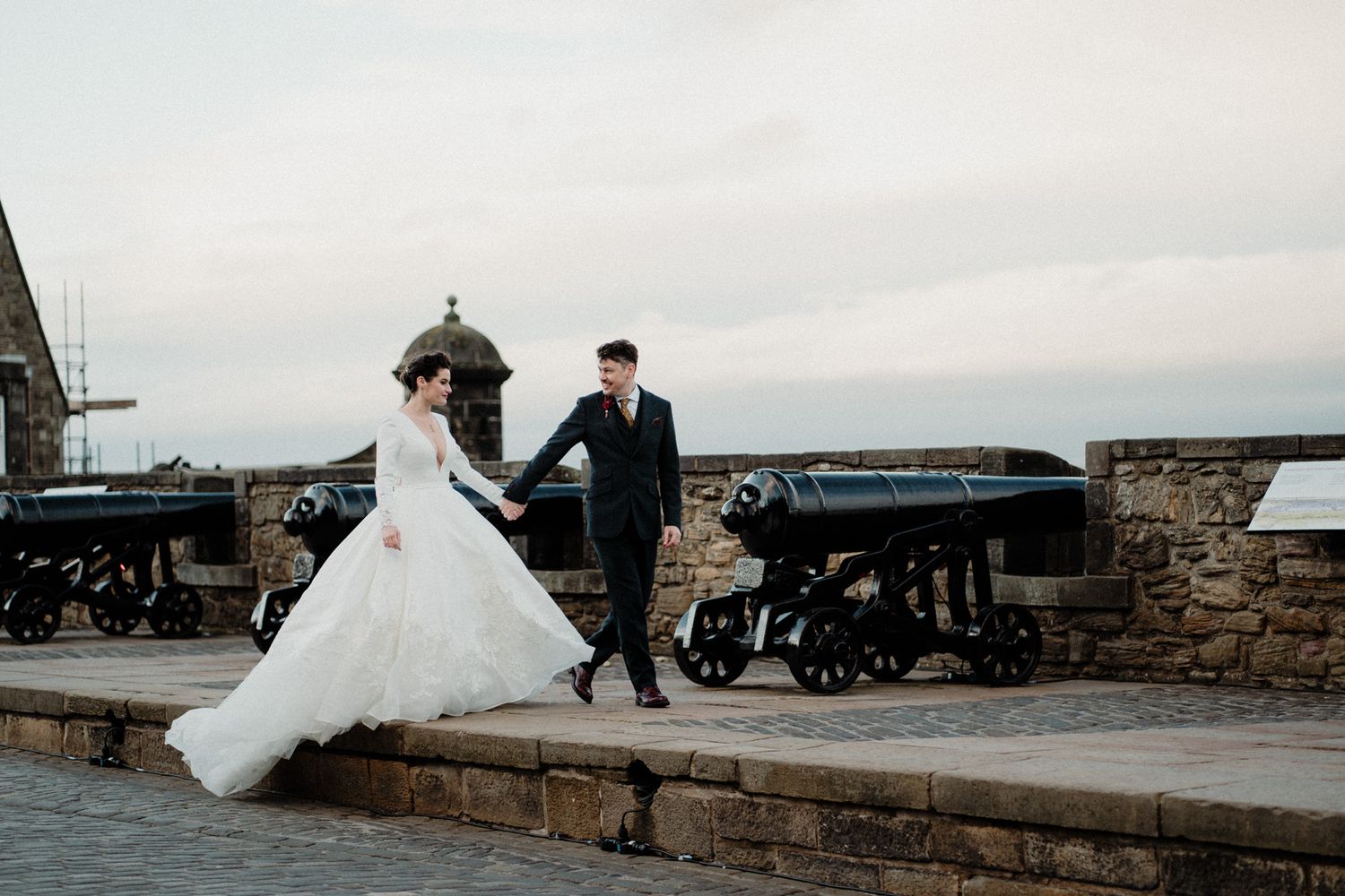 Wedding couple walking along a stone wall with vintage cannons at sunset.