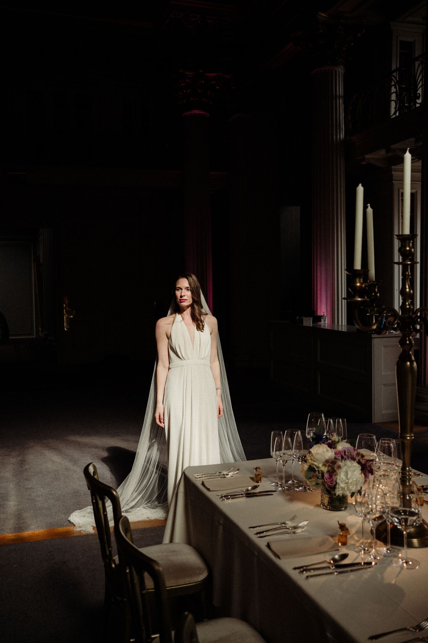 Elegant dining table setup with candlelight and place settings in a dark moody atmosphere with soft lighting.