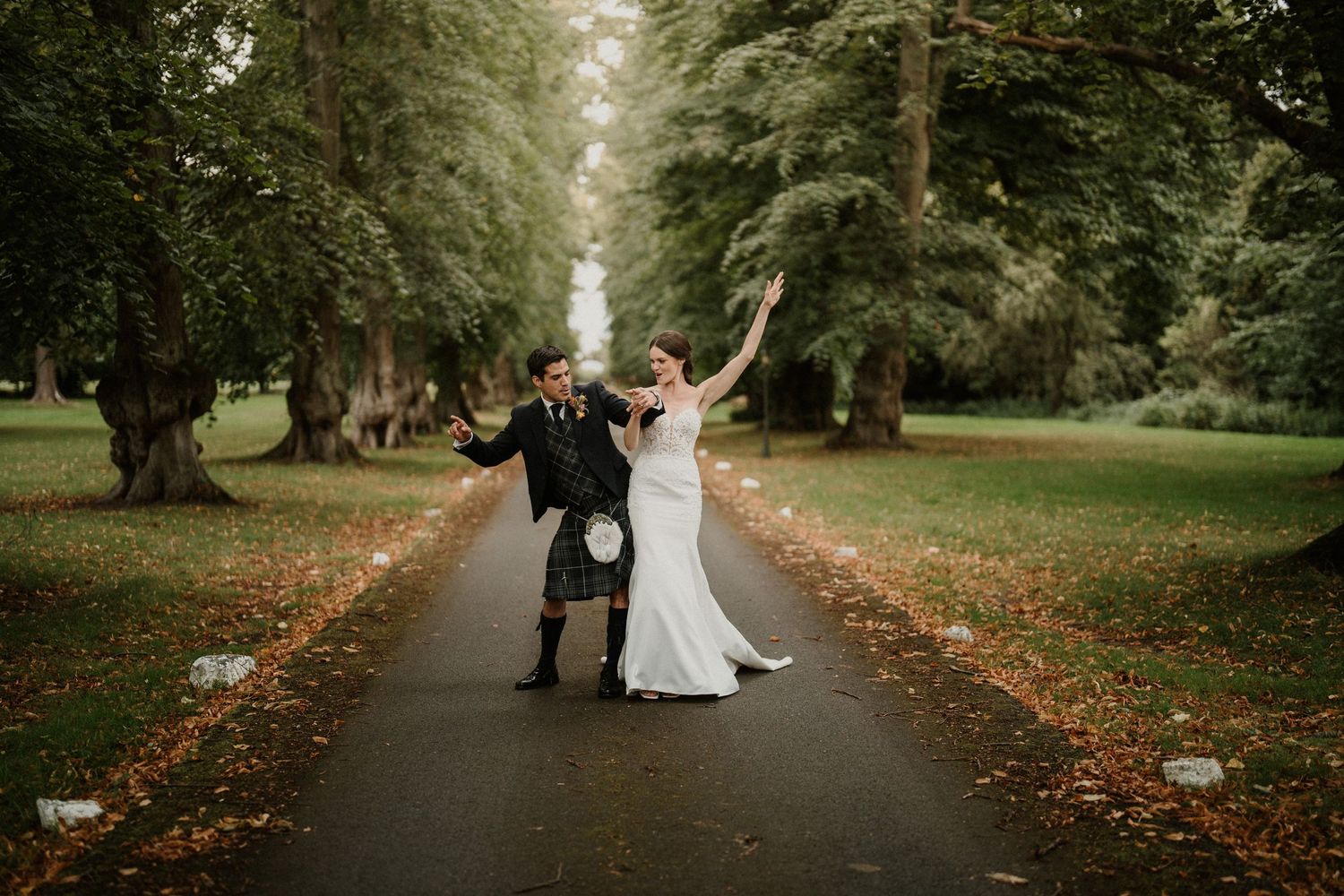 Autumn wedding photo shoot along a tree-lined path with fallen leaves.