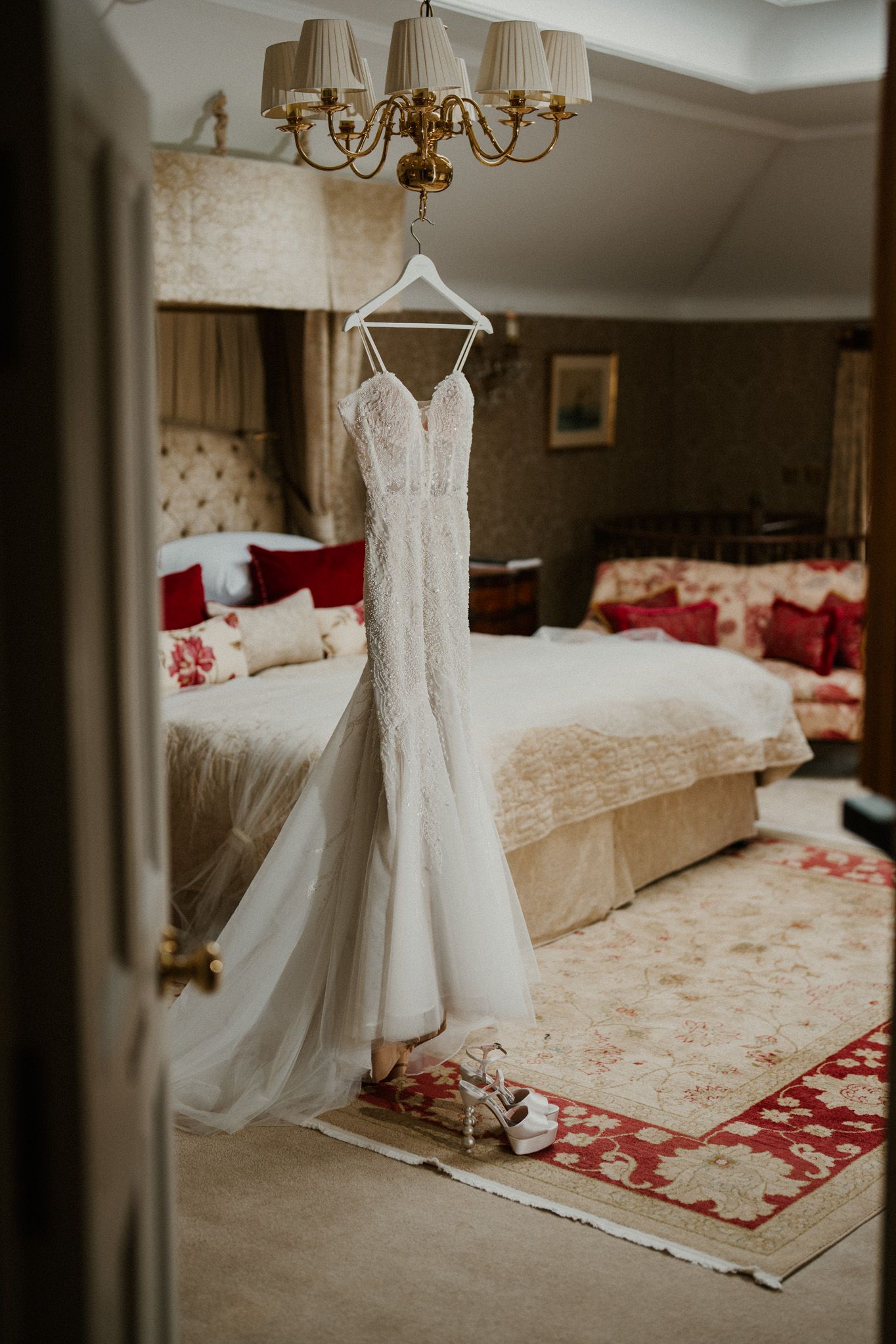 White lace wedding dress hanging in an elegant room with a red patterned rug.