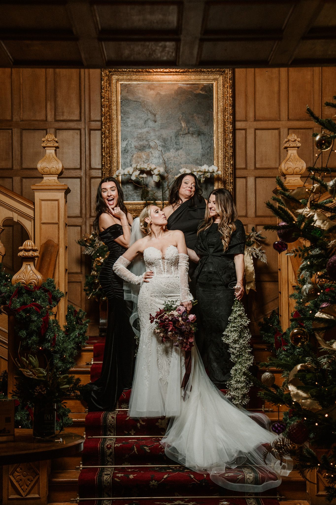 Wedding party gathered on decorated staircase with wood paneling and holiday greenery.