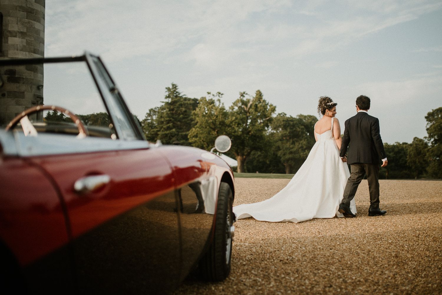 Artistic wedding photography featuring castle architecture and vintage car at sunset.