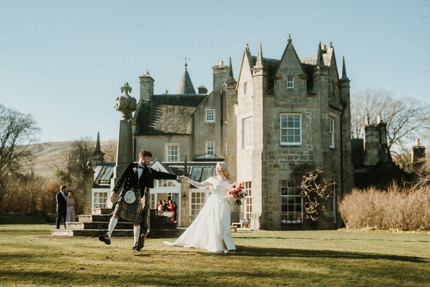 Newlyweds celebrate outside a Scottish castle with a joyful jumping photo.