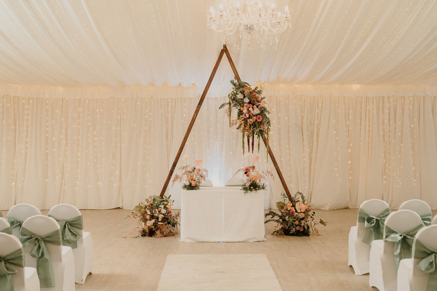 Elegant white wedding reception tent with chandeliers and draped fabric decor.