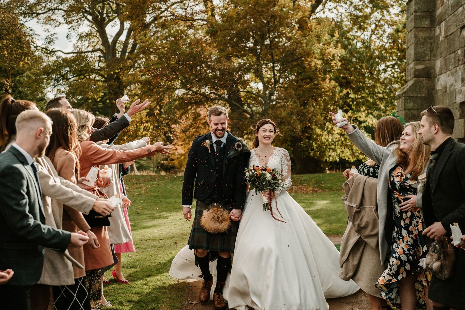 Wedding guests celebrate outdoors under autumn trees during a joyful reception ceremony.