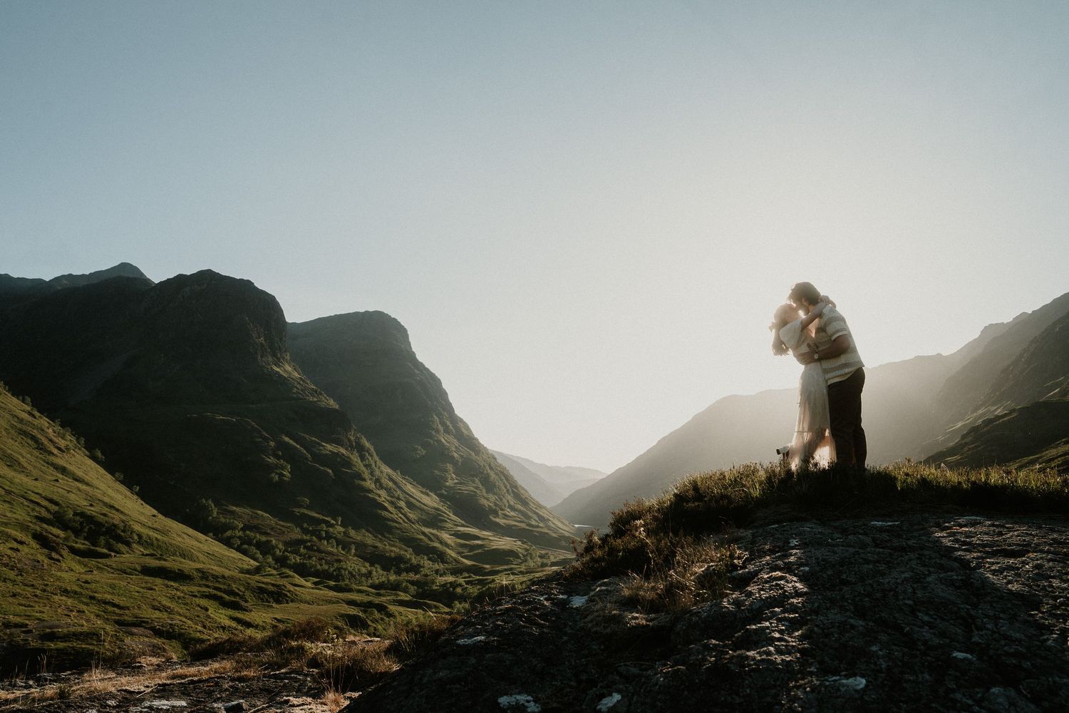 Romantic mountain landscape photography with couple silhouetted against setting sun.