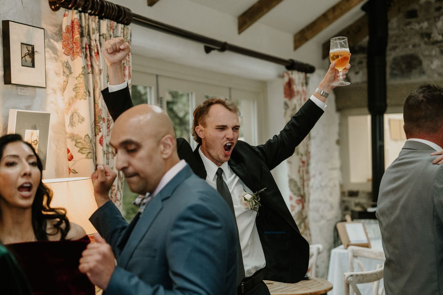 Wedding guests celebrate enthusiastically during the reception in a rustic stone venue.