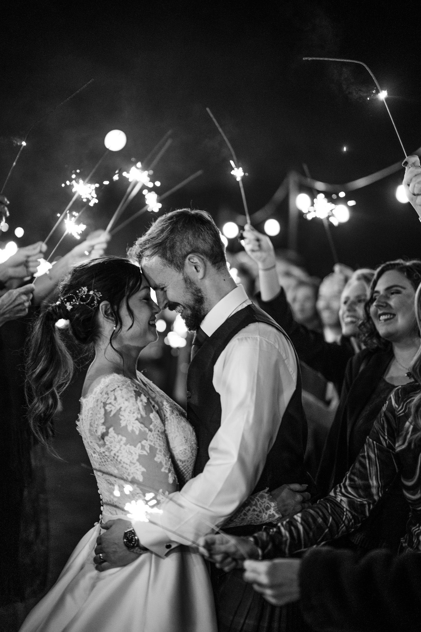Black and white capture of a sparkler-filled wedding celebration under the night sky.