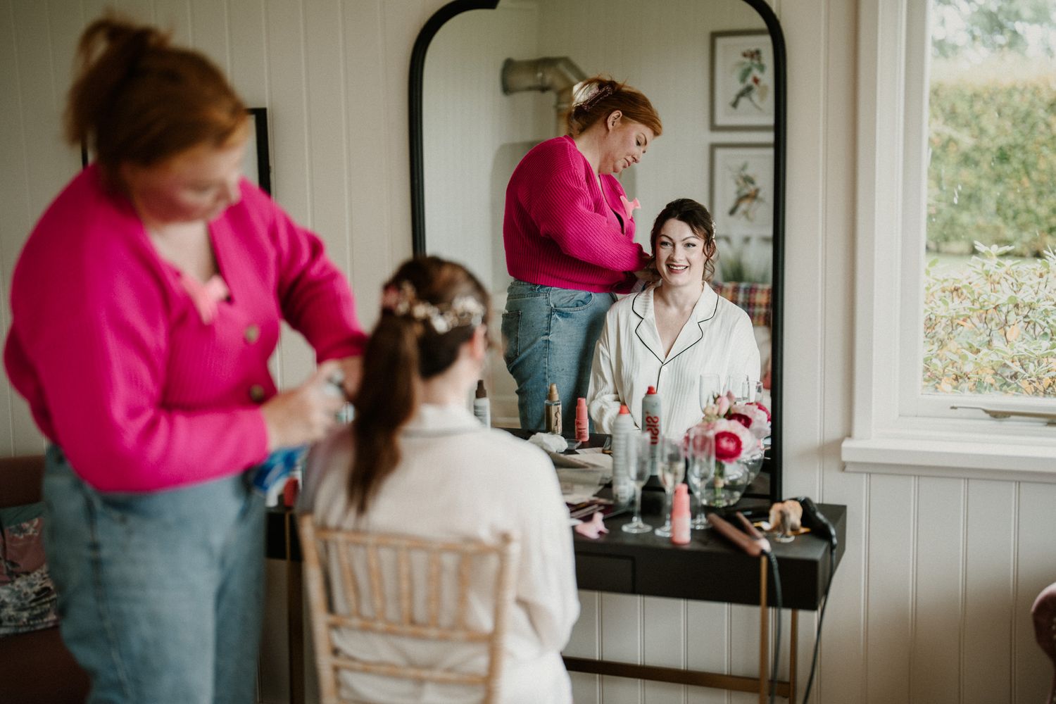 People in formal attire prepare in a bright interior room with white paneled walls.