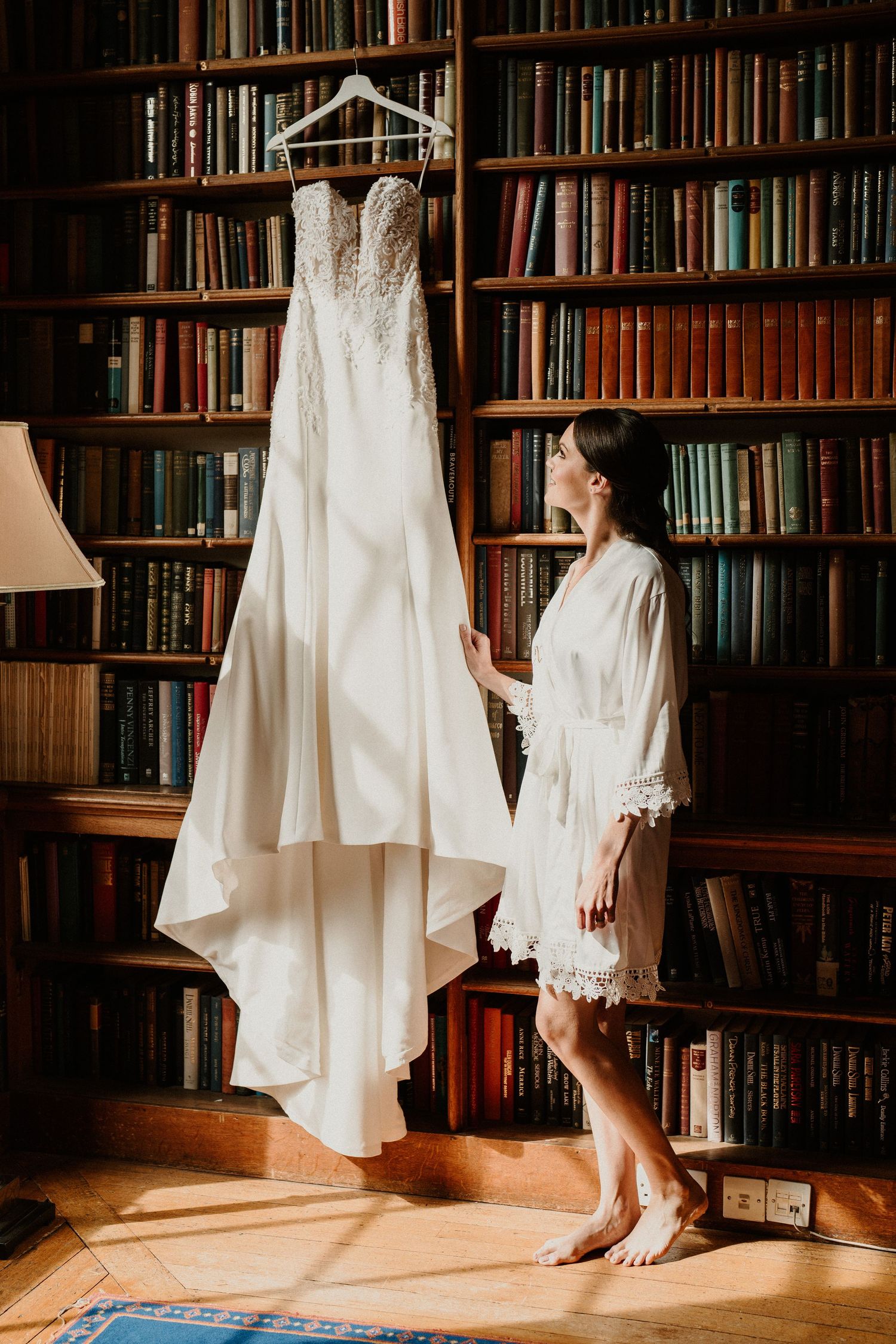 White wedding dress hanging in a library against dark wooden bookshelves.
