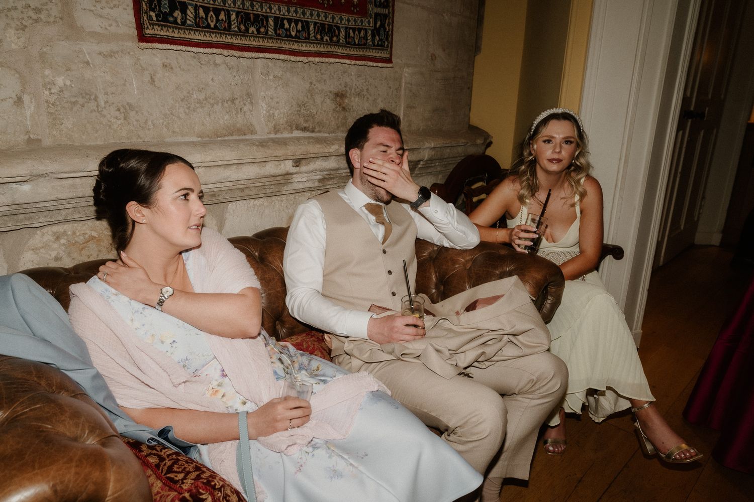 Wedding party relaxing on a vintage sofa, bride and groom sharing a candid moment with guests at a elegant venue.