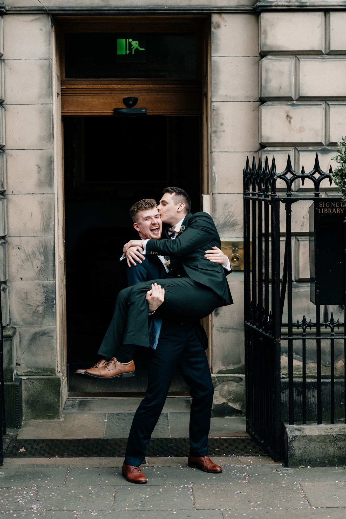 Playful wedding photos taken outside historic stone building with iron gates.