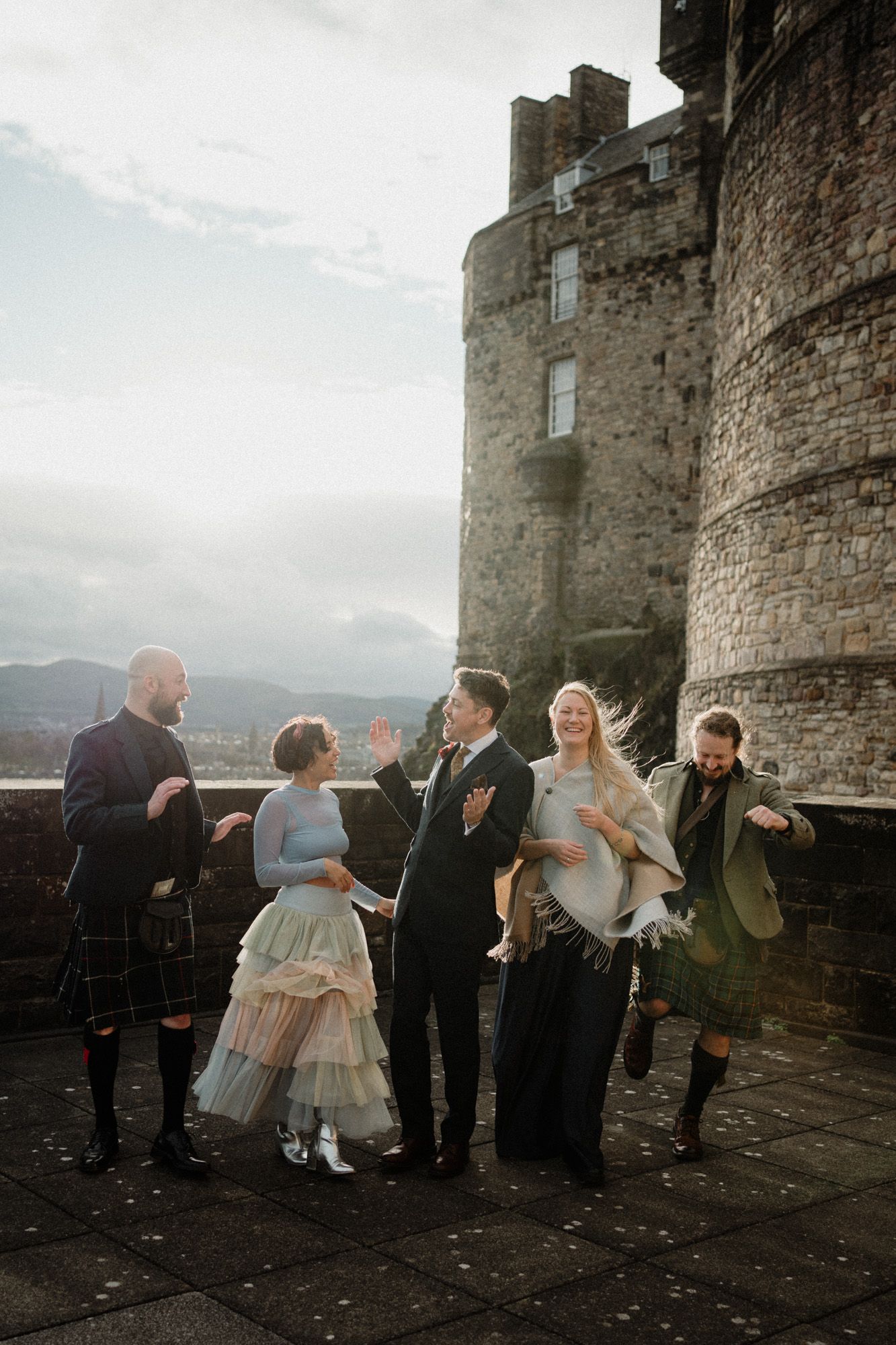 Wedding party gathers along stone castle walls under moody skies in Scotland.