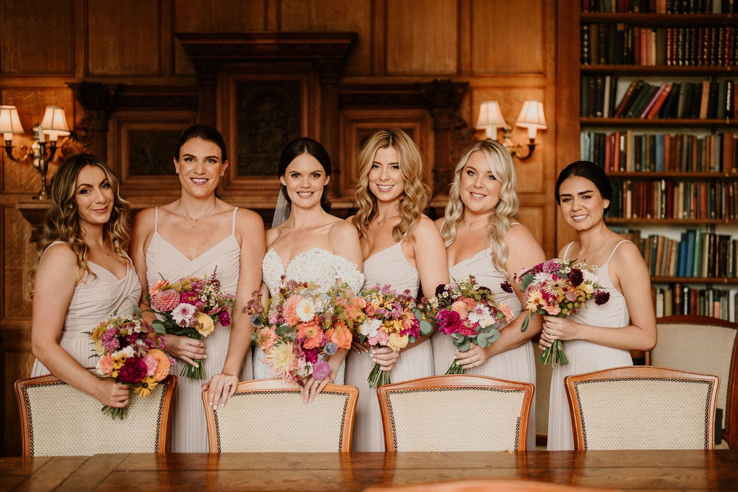 Wedding party poses together in elegant library setting with warm lighting and wooden bookshelves.