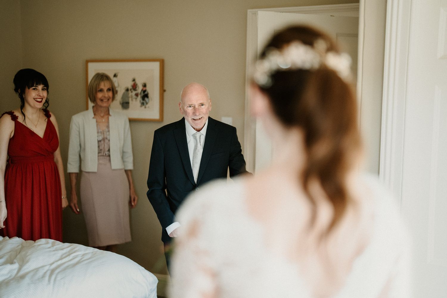 Wedding preparation scene with various people in formal attire gathered in a room.