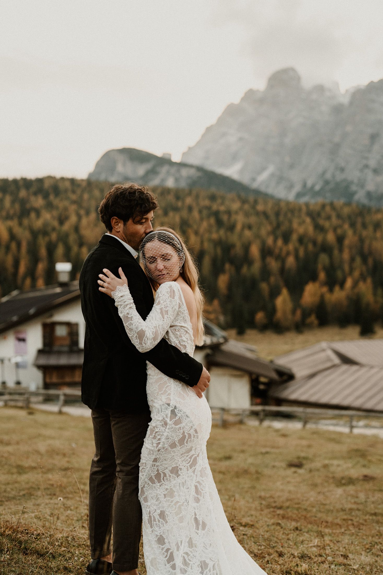 A romantic embrace on a mountain meadow with dramatic alpine peaks and golden larches in the background.