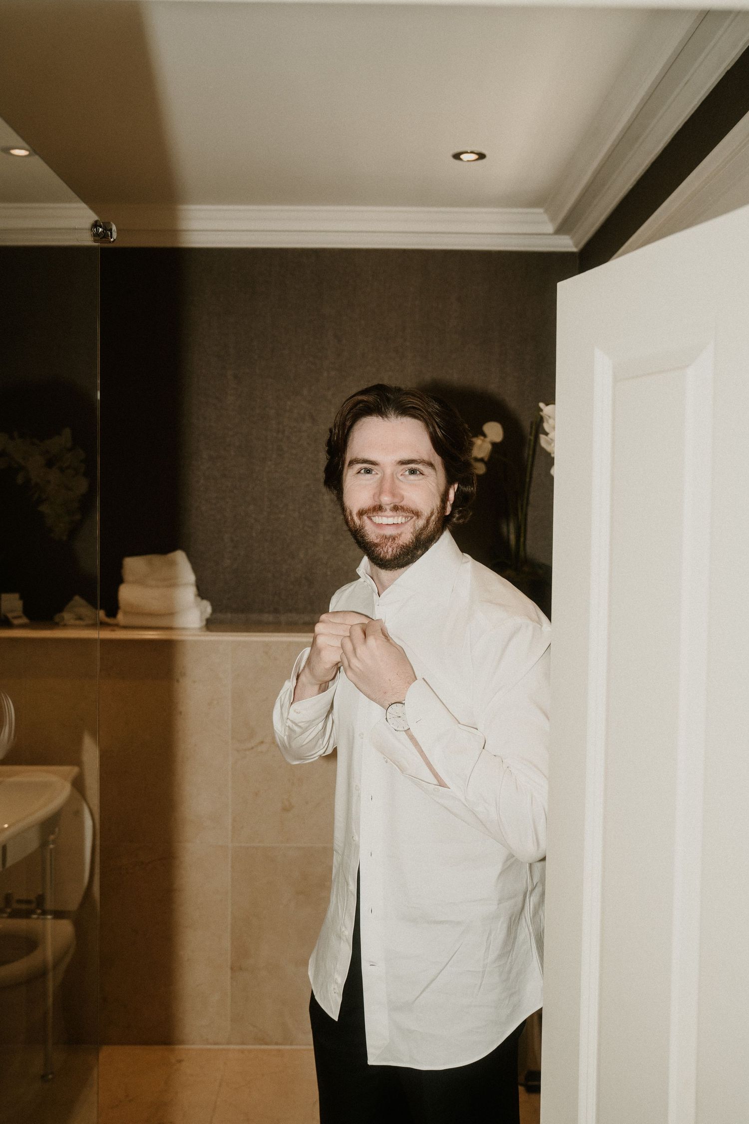 Someone in white formal attire smiling and posing in an interior hallway.