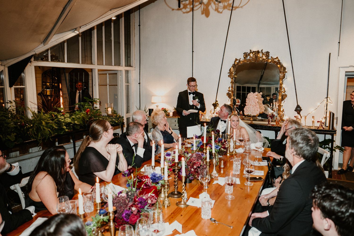Long dining tables set with candles and floral arrangements at an upscale wedding reception.