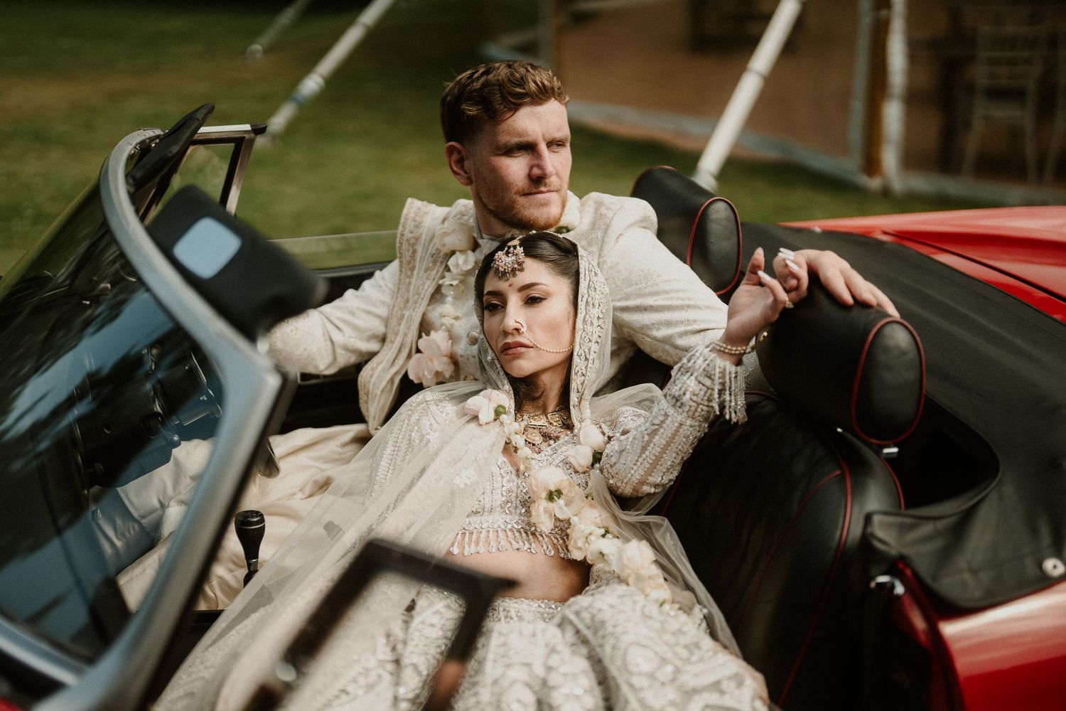 Artistic wedding photography featuring couple in classic red convertible car.