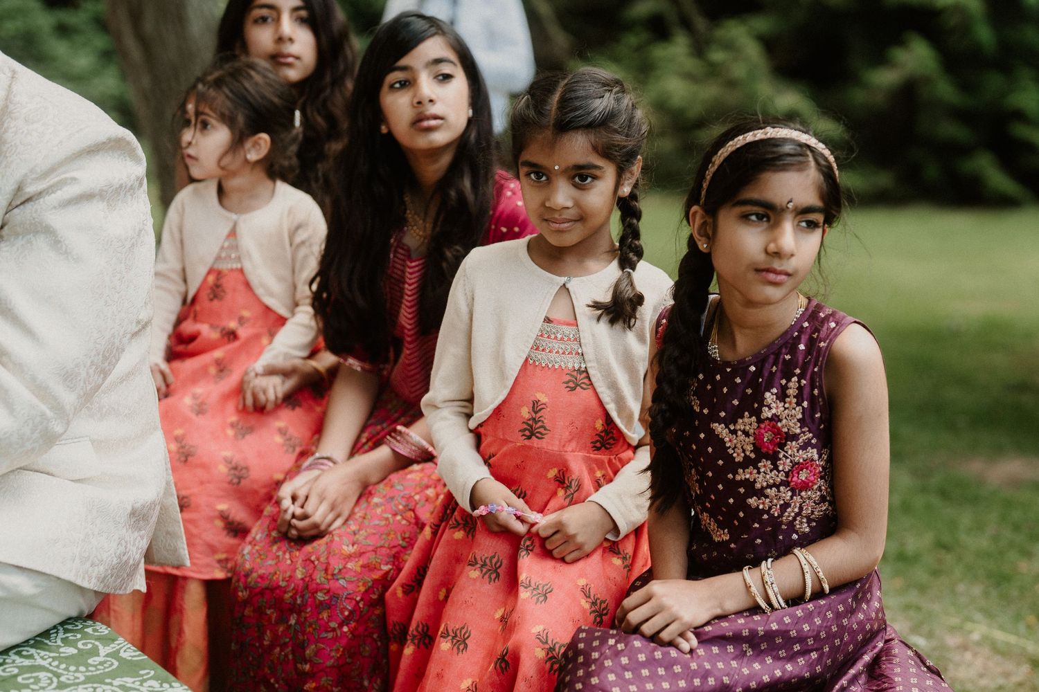 Young attendants in coral and burgundy dresses gather for wedding party photos on the lawn.